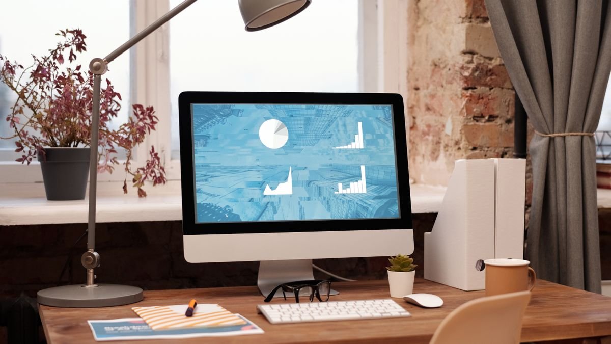 Werkplek met iMac, bureaulamp en plant bij een bakstenen muur