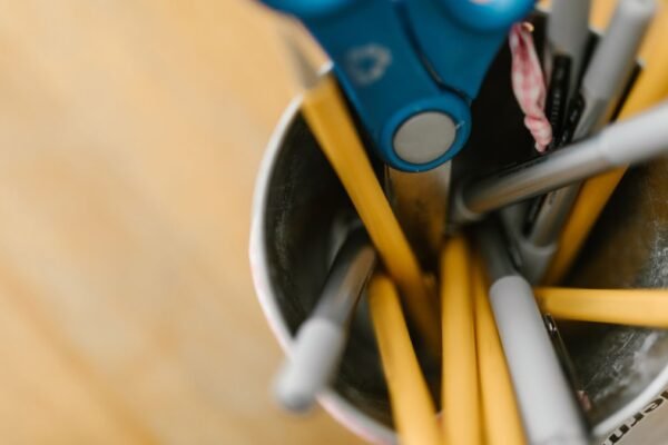 Metalen pennenhouder met schaar en pennen op houten bureau