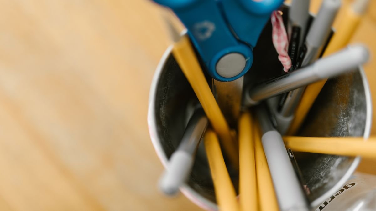 Metalen pennenhouder met schaar en pennen op houten bureau