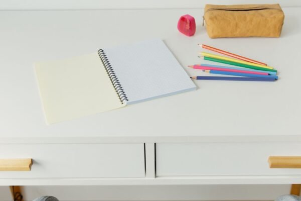 Notitieboek met kleurpotloden op wit kinderbureau